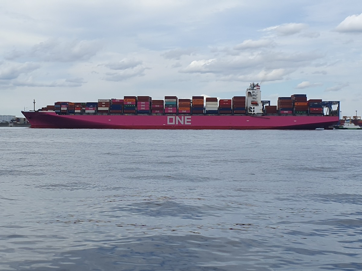 A large container ship loaded with colourful shipping containers, identified as the ONE (Ocean Network Express), entering a harbour.